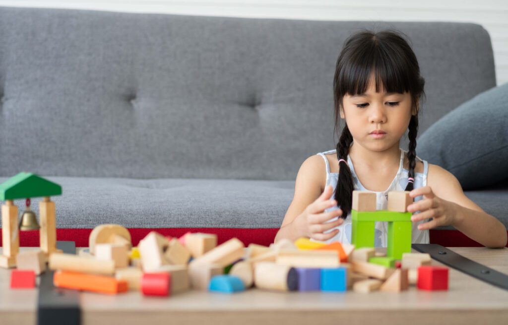 Cute Asian little girl playing with colorful toy blocks